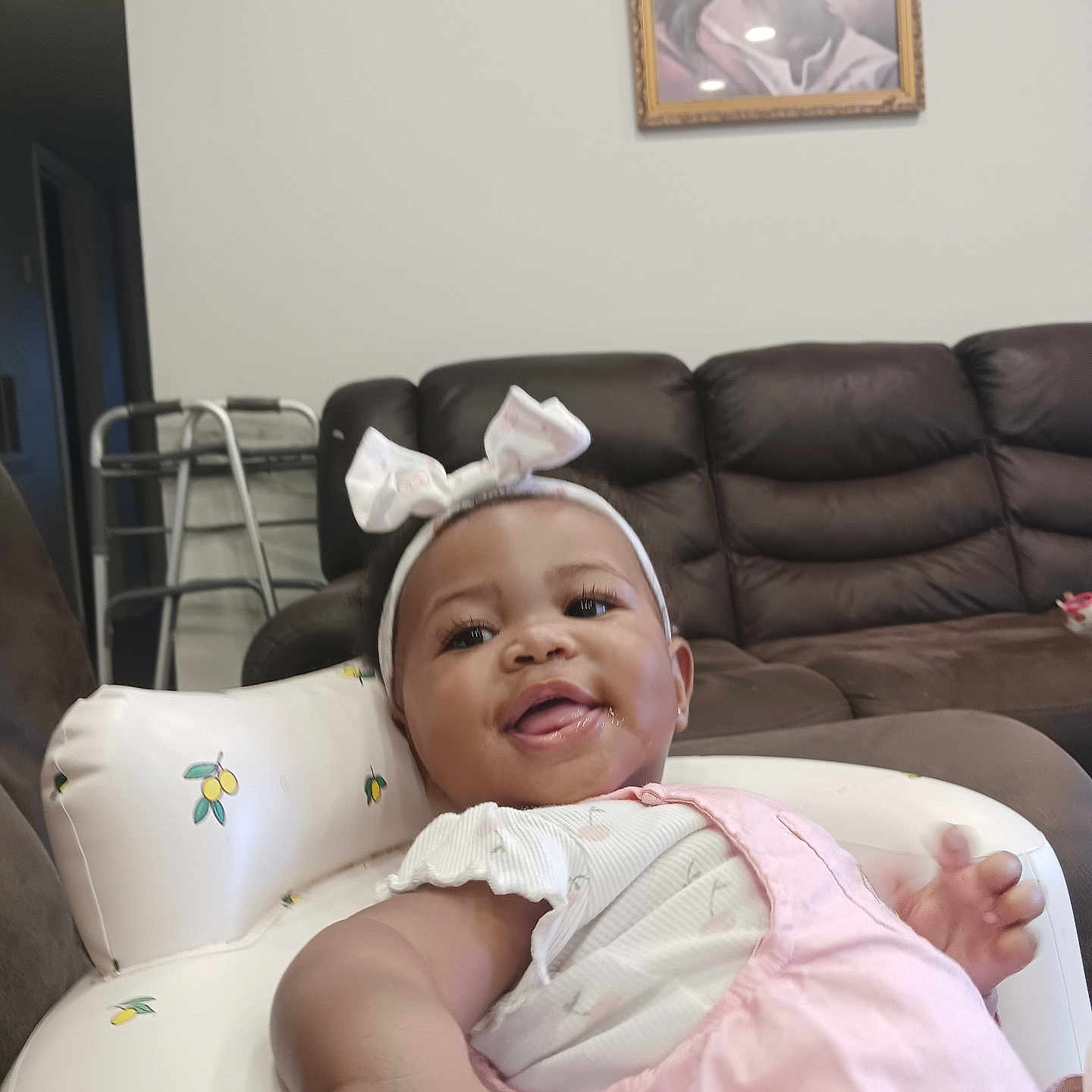 Skylah joined the competition — help win amazing prizes! baby, infant, child, smiling, tongue_out, headband, bow, pink_clothing, romper, sitting, reclining, baby_seat, cushion, living_room, sofa, furniture, indoor, portrait, framed_picture, home