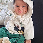 Rafael participe au concours pour gagner de l'argent avec cette photo : baby, child, hoodie, smile, cute, green_pants, white_clothing, face, person, indoor, blanket, sitting, happy, clothing, infant, cozy, lap, soft_toy, hood, casual