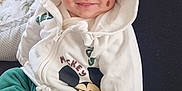 Rafael participe au concours pour gagner de l'argent avec cette photo : baby, child, hoodie, smile, cute, green_pants, white_clothing, face, person, indoor, blanket, sitting, happy, clothing, infant, cozy, lap, soft_toy, hood, casual