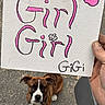 animal, art, brown_dog, canine, collar, dog, hand, handwritten_text, holding, leash, looking_up, outdoor, painting, pavement, paw_print, person_hand, pet, sign, text, white_markings