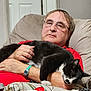 armchair, beige, black_and_white_cat, casual, cat, comfort, companion, furniture, glasses, hand, home, indoor, man, person, pet, red_shirt, relaxed, resting, sleeping_cat, watch