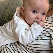 Anaë a rejoint le concours — aidez-le/la à gagner de superbes lots ! baby, infant, child, couch, striped_clothing, hand_in_mouth, blue_eyes, face, person, indoors, pillow, cozy, sitting, cute, portrait, head, sleepsuit, soft_texture, relaxing, home