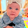 baby, child, blue_eyes, headband, bow, play_mat, colorful, curious, infant, cute, hands, face, clothing, portrait, indoors, soft_lighting, expression, closeup, toddler, smile