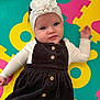 baby, headband, flower, blue_eyes, corduroy_dress, wooden_buttons, cream_shirt, foam_puzzle_mat, colorful_background, laying_down, child, infant, cute, portrait, indoors, soft_lighting, happy, smiling, hand, person