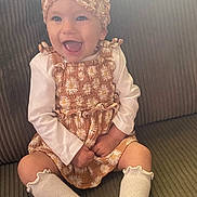 Alynnah is registered to the contest to win money with this photo: baby, child, smiling, headband, socks, couch, seated, happy, portrait, clothing, infant, cute, indoors, person, fabric, textured, daisy_pattern, long_sleeve, casual, young