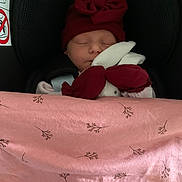 Joy a rejoint le concours — aidez-le/la à gagner de superbes lots ! baby, sleeping, car_seat, red_hat, bow, blanket, pink_blanket, plush_toy, bunny_toy, child, infant, cozy, cute, peaceful, face, headwear, soft_toy, resting, indoors, safe