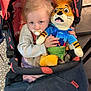 child, stroller, pacifier, plush_toy, tiger_toy, flamingo_pattern, clothing, indoor, cute, baby, toy, fabric, seat, comfort, person, blond_hair, hand, face, sitting, expression