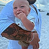 baby, child, man, tattoo, beach, sand, sky, clouds, blue_eyes, smile, chewing, holding, white_shirt, bracelet, portrait, outdoor, person, happy, summer, family