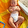 baby, towel, toy, diaper, beach, sand, sunlight, smile, barefoot, orange, yellow, infant, relaxing, child, outdoor, cute, skin, playful, summer, lying_down
