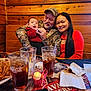 baby, camouflage, candle, coca_cola, drink, family, fried_food, glasses, hat, indoor, man, napkins, plate, portrait, red_sweater, restaurant, smiling, table, woman, wooden_wall