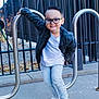 Asher joined the competition — help win amazing prizes! child, boy, glasses, jacket, jeans, sneakers, outdoor, playful, smile, bike_rack, sidewalk, fence, casual_clothing, young, posing, happy, street, urban, daylight, person