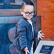 Asher joined the competition — help win amazing prizes! child, boy, glasses, jacket, jeans, outdoor, sculpture, plaque, brick_wall, pose, smile, hands, fashion, casual, young, person, portrait, daylight, expression, playful