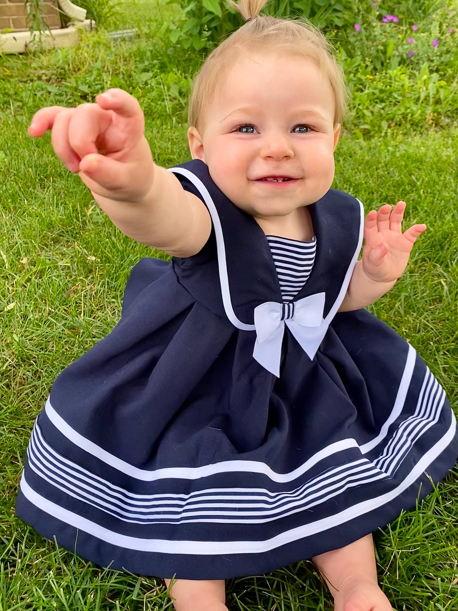 Rowan is registered to the contest to win money with this photo: baby, baby_toddler_clothing, clothing, face, finger, formal_wear, gesture, grass, hand, happy, head, joy, outerwear, people_in_nature, person, plant, sitting, sleeve, smile, thumb