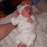 Waylon is registered to the contest to win money with this photo: baby, newborn, child, pajamas, hand, blanket, bed, sleeping, infant, foot, adult_arm, comfort, indoor, clothing, rest, soft, peaceful, family, care, gentle_touch