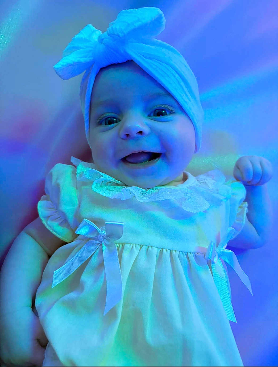 Novah-Seren is registered to the contest to win money with this photo: baby, infant, smiling, headwrap, dress, bow, cute, happy, portrait, closeup, child, blue_light, purple_light, fabric, clothing, face, eyes, hand, skin, indoors