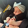 baby, sleeping, car_seat, headband, white_headband, bow, hand, holding, infant, child, seatbelt, black, closeup, peaceful, resting, human, skin, cute, toddler, transportation