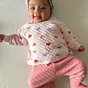 Mélissa a rejoint le concours — aidez-le/la à gagner de superbes lots ! baby, child, pink_clothing, heart_pattern, headband, flower_headband, tongue_out, lying_down, happy, cute, infant, sweater, pants, socks, playful, indoors, smiling, portrait, one_person, white_background