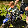Wyatt is registered to the contest to win money with this photo: child, toddler, dirt_bike, blue, outdoor, grass, person, tattoo, shorts, sneakers, sunlight, motorbike, number_23, handlebars, curious, supporting_hand, greenery, daytime, casual_clothing, small_vehicle