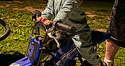 Wyatt is registered to the contest to win money with this photo: child, toddler, dirt_bike, toy_vehicle, grass, night, adult_hand, tattoo, playful, outdoor, happy, motorbike, small_vehicle, person, fun, clothing, footwear, dark_background, illuminated, tongue_out