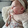 baby, pacifier, headband, knit_sweater, floral_embroidery, pillow, couch, indoor, child, cozy, soft_texture, seated, cute, infant, side_profile, casual_clothing, relaxed, small_hand, comfort, portrait