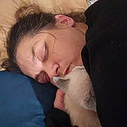 Albus Theodore is registered to the contest to win money with this photo: person, sleeping, cat, pet, pillow, blanket, bed, cuddle, cozy, indoor, portrait, closeup, hair, ear, nose_piercing, hand, fur, blue_pillow, black_jacket, nap