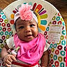 baby, smiling, headband, pink_bib, baby_seat, colorful_pattern, elephant_design, hand, clip, infant, face, cute, indoors, wood_floor, happy, child, portrait, toddler, clothing, seat