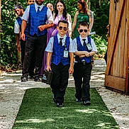 Hunter is registered to the contest to win money with this photo: children, boys, wedding, ring_bearers, sunglasses, formalwear, vests, suits, bow_ties, outdoor, wooden_gates, forest, green_carpet, wedding_party, ceremony, walking, portrait, sunlight, family, celebration
