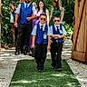 children, boys, wedding, ring_bearers, sunglasses, formalwear, vests, suits, bow_ties, outdoor, wooden_gates, forest, green_carpet, wedding_party, ceremony, walking, portrait, sunlight, family, celebration