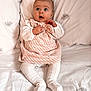 baby, infant, child, dress, white_clothing, patterned_fabric, bed, pillow, leaf_pattern, soft_texture, sitting, curious_expression, wide_eyes, hands, legs, indoors, portrait, cute, cozy, comfortable