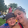 child, woman, smile, selfie, outdoor, grass, tree, people, cap, hat, casual_clothing, blue_sky, sunlight, happy, portrait, nature, event, relaxation, family, fun
