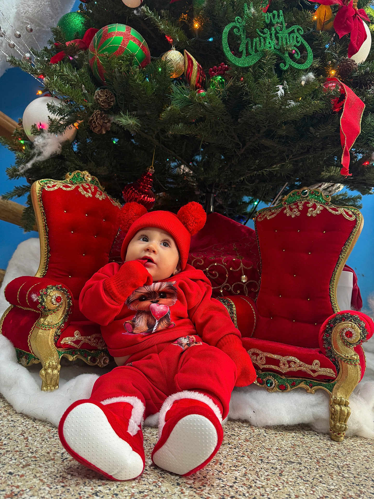 Emily joined the competition — help win amazing prizes! baby, child, christmas_tree, red_clothing, hat, booties, holiday, decorations, ornate_chair, festive, indoors, floor, pom_pom, cute, seasonal, celebration, smiling, winter_wear, home, festivity