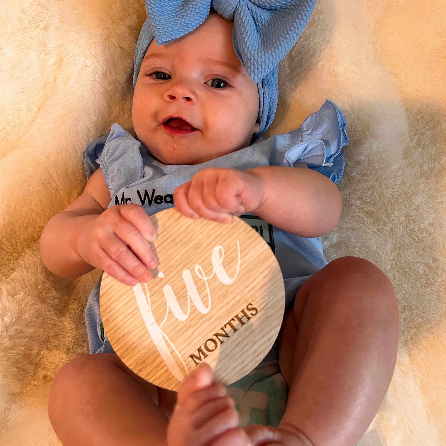 Magnolia is registered to the contest to win money with this photo: baby, infant, blue_bow, headband, blue_clothing, wooden_plaque, five_months, drool, blanket, soft_texture, cute, lying_down, hands, feet, skin, portrait, smile, indoor, person, child
