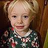 child, girl, blonde_hair, pigtails, smile, sweater, candy_cane, snowflake, holiday_clothing, portrait, indoors, wooden_background, happy, cute, face, person, young_child, festive, christmas_theme, casual