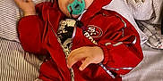 Jacob Corona is registered to the contest to win money with this photo: baby, child, pacifier, red_jacket, red_pants, striped_bedspread, bed, blanket, indoor, infant, cute, clothing, person, young_child, relaxed, lying_down, casual, cozy, comfort, hooded_jacket