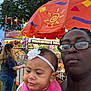 Kelisia joined the competition — help win amazing prizes! baby, woman, glasses, headband, umbrella, carnival, fairground, outdoor, people, clothing, food_stall, trees, sky, fence, pink_bib, portrait, daylight, crowd, person, festival
