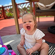 Navy joined the competition — help win amazing prizes! toddler, child, toy, outdoor, deck, table, striped_rug, hand, foot, white_clothing, sunlight, happy, playful, person, smiling, barefoot, wooden_furniture, summer, blue_sky, expression