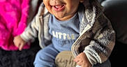 Kairo joined the competition — help win amazing prizes! baby, child, smiling, sitting, blue_clothing, jacket, sock, face, portrait, indoor, blanket, pink, happy, cute, infant, cozy, soft, furniture, person, closeup