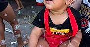 Kairo joined the competition — help win amazing prizes! baby, background, barefoot, black_shirt, bubbles, casual, child, curly_hair, daylight, earrings, face, hand, lap, legs, outdoor, people, person, red_clothing, smiling, toddler