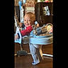 activity_center, baby, brick_wall, child, face, floor, furniture, happy, home, indoor, legs, person, play, red_shirt, shelf, sitting, smiling, socks, toddler, toy