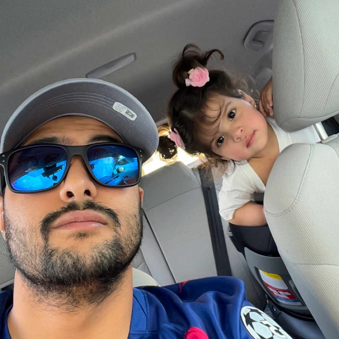 Elaina Amirah Beloua joined the competition — help win amazing prizes! man, child, car, selfie, sunglasses, cap, hair_clip, seat, backseat, curious, portrait, casual, family, interior, clothing, beard, young_child, blue_shirt, pink_accessory, daylight