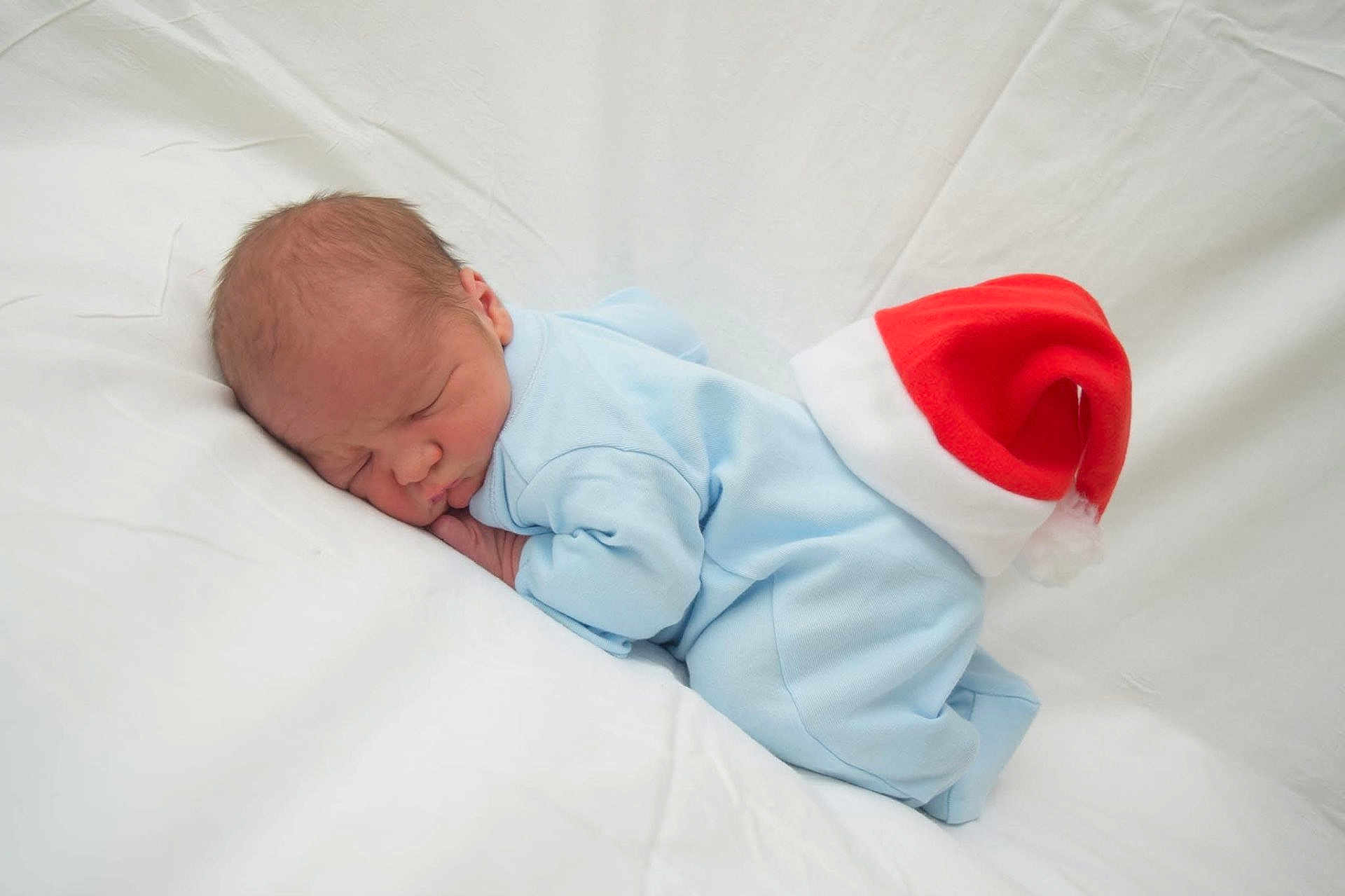 Ronan-James is registered to the contest to win money with this photo: newborn, baby, sleeping, blue_onesie, white_blanket, santa_hat, holiday, cute, infant, resting, soft_fabric, peaceful, portrait, indoors, child, cozy, small, face, head, skin
