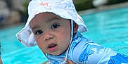 Zakkai is registered to the contest to win money with this photo: baby, child, swimming_pool, water, hat, sun_hat, blue, swimsuit, shark_pattern, person, outdoor, summer, water_activity, holding, face, headwear, recreation, skin, cute, expression