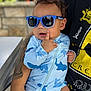 Zakkai is registered to the contest to win money with this photo: baby, blue_sunglasses, swimwear, shark_pattern, tattoo, adult_arm, table, outdoor, child, person, sitting, face, hand, clothing, casual, sun_protection, cute, portrait, expression, reflection