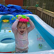 Paisley joined the competition — help win amazing prizes! toddler, inflatable_pool, water_toy, backyard, child, swimsuit, summer, playful, smiling, water, toy, fence, plastic, outdoor, happy, splashing, colorful, sunlight, nature, fun
