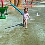 toddler, child, water_park, splash_pad, water_fountain, pool_noodle, playground, outdoor, summer, fun, sunny, water_spray, footwearless, play, recreation, baseball_glove_sculpture, greenery, trees, water, happiness