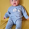 baby, blue_outfit, bright_background, casual, child, comfortable, cozy, cute, elephant_design, happy, home, indoor, infant, looking_at_camera, portrait, seated, smiling, soft_clothing, yellow_couch, young_child