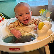Jayden is registered to the contest to win money with this photo: baby, child, smiling, laughing, activity_center, toy, indoor, playtime, infant, happy, cute, person, seat, colorful, furniture, curtains, clothing, hands, face, expression