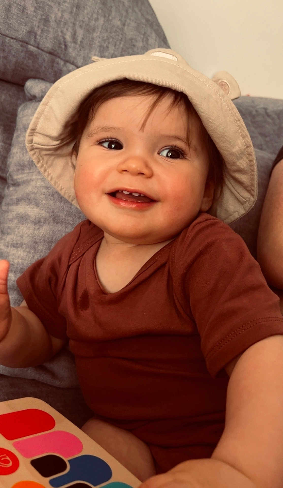 Malone a rejoint le concours — aidez-le/la à gagner de superbes lots ! toddler, child, smiling, hat, bucket_hat, brown_shirt, toy_piano, colorful, indoor, couch, happy, playful, cute, infant, face, person, seated, furniture, home, young_child