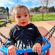 Kais participe au concours pour gagner de l'argent avec cette photo : child, toddler, swing, playground, outdoor, park, fence, bench, grass, sky, clouds, person, jacket, nike, hands, face, expression, daylight, casual_clothing, chains