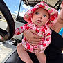 baby, infant, child, strawberry_hat, sun_hat, pink_outfit, patterned_clothing, hand_holding, adult_hand, golf_cart, steering_wheel, seat, sky, clouds, outdoor, portrait, cute, ring, bare_legs, person